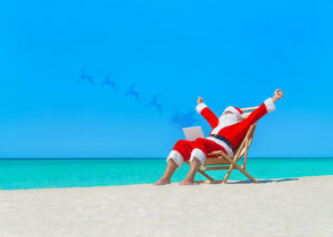 Weihnachtsmann am Strand schickt seine Rentiere auf Reise vom Laptop aus